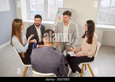 Group of young business professionals sitting in circle and sharing ideas during office team meeting Stock Photo