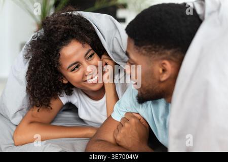 Happy couple lying in bed under blanket Stock Photo