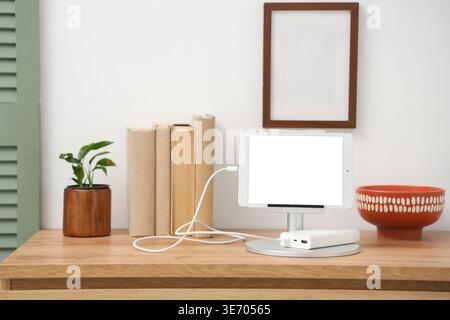 Tablet computer charging from power bank on shelf in room Stock Photo