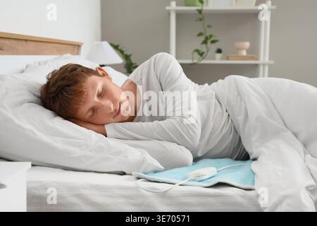 Young man sleeping on electric heating pad in bedroom Stock Photo