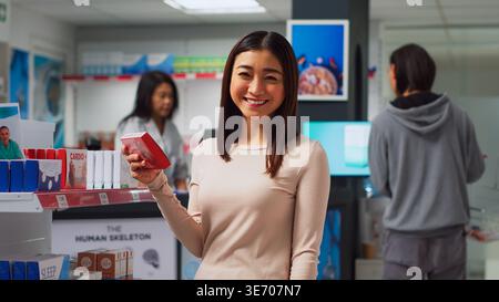 Woman customer taking vitamins box off drugstore shelves, searching for medicaments and pills in package. Young person looking at healthcare supplements and pharmaceutical products. Stock Photo