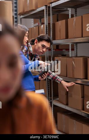 Warehouse employees inspecting parcels on rack and doing inventory management. Storehouse asian package handler and supervisor checking goods maintenance on shelf in storage room Stock Photo