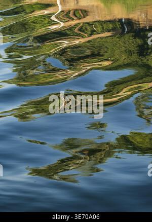 A small sailboat floats on a calm river Nile, its reflection distorted by gentle ripples creating an abstract pattern on the water's surface Stock Photo