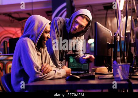 Hackers smiling while cracking encrypted information successfully on computer and working together in hideout place. Two criminals coding illegal malicious software for server hacking Stock Photo