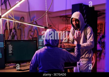 Smiling african american criminal discussing plan to break into computer network system. Two cheerful hackers talking about ransomware attack on company database to steal confidential information Stock Photo