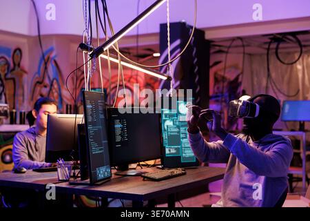 Criminal hacking using vr technology and breaking into server while exploring metaverse. Hacker in virtual reality headset doing illegal activity and programming malicious software Stock Photo