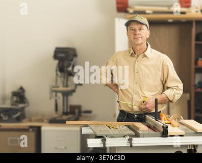 Senior man working on tools in home workshop with table saw, bench drill and other equipment Stock Photo