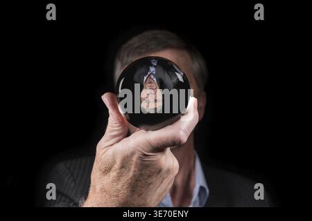 Senior caucasian hand holding glass sphere with upside down reflection of head. Concept for fear of change, new reality or world upside down Stock Photo