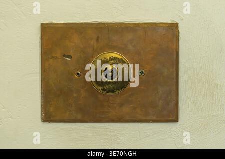 Close up of antique toggle light switch with copper faceplate on textured concrete wall providing vintage, rustic design detail Stock Photo