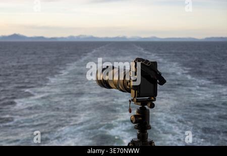 Professional dslr on tripod on back of cruise ship sailing away from Alaska coast leaving wake Stock Photo
