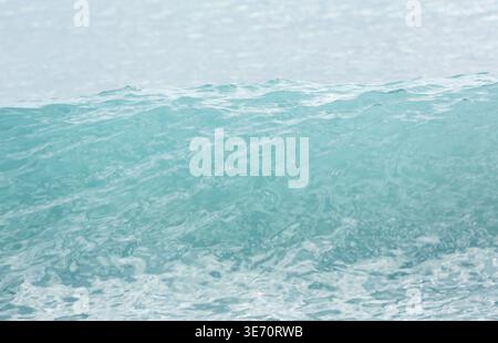 Turquoise blue wave building to peak before breaking as surf on the shore Stock Photo