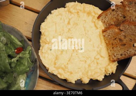 Delicious scrambled eggs served with bread and salad Stock Photo