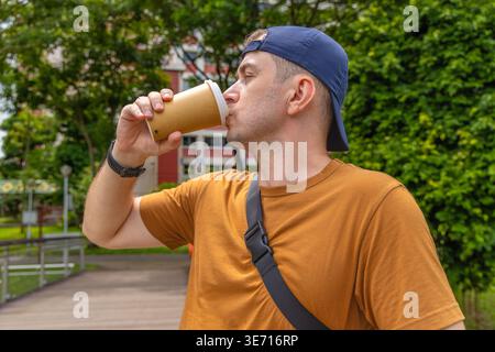 Man drinking coffee from takeaway paper cup in urban park during day shot as medium profile view Stock Photo