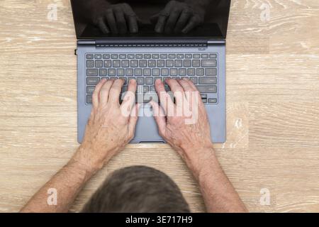Senior caucasian adult man typing on laptop keyboard on wooden desk in photo taken from above Stock Photo