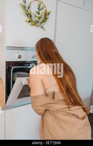 Woman oven cooking young woman checking food inside a modern appliance in a bright minimalist kitchen Stock Photo