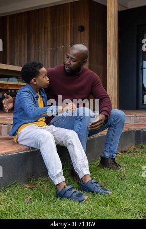 African American father and son sitting on brick steps talking, father wearing maroon sweater Stock Photo