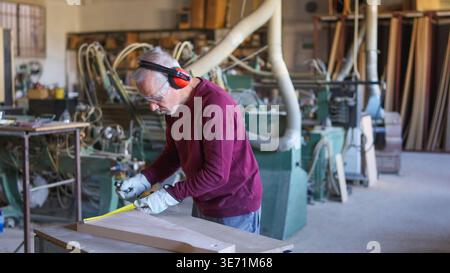 Experienced carpenter measuring wood in woodworking workshop Stock Photo