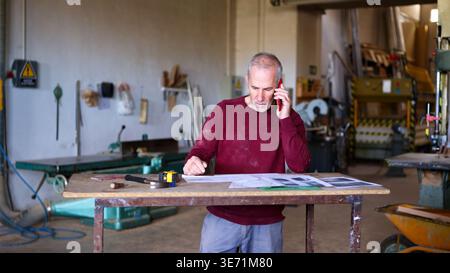 Senior woodworker managing small business with phone call Stock Photo