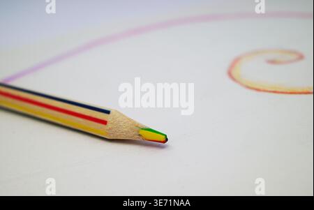 Multicolored pencil, featuring striped edges in blue, yellow, and red. Its tip combines green, yellow, and red shades. The pencil lies on white paper Stock Photo
