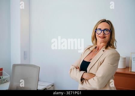 Confident businesswoman smiling, crossing arms in a modern office environment Stock Photo