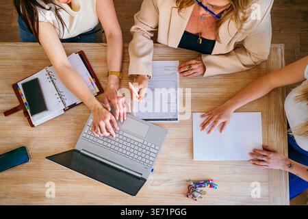 Three businesswomen working together with a laptop and documents on a wooden table Stock Photo