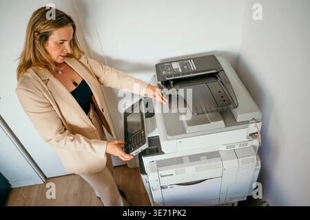 Businesswoman operating a large copy machine in an office setting Stock Photo