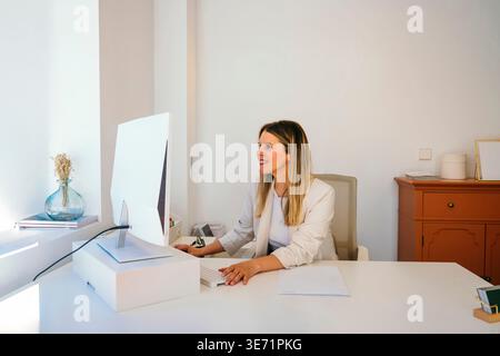 Woman using a desktop computer at a white desk in a modern office setup Stock Photo