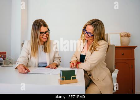 Two businesswomen reviewing important documents together, discussing agreement in a bright office Stock Photo