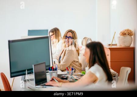 Women working at computers in a shared office space, smiling and interacting Stock Photo