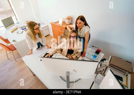 Businesswomen collaborating and communicating while checking a computer screen in a modern office setup Stock Photo