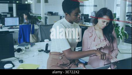 Collaborating two women in light top and pink blouse, leaning on desk in office sharing tablet. Teamwork, workspace, openplan, monitors, devices, head Stock Photo