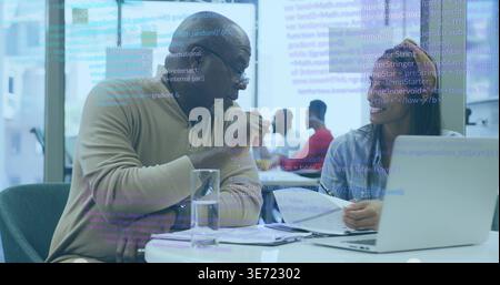 Explaining code colleagues in tan sweater and light top holding papers at office viewing laptop. Coworking, collaboration, meeting, teamwork, technolo Stock Photo