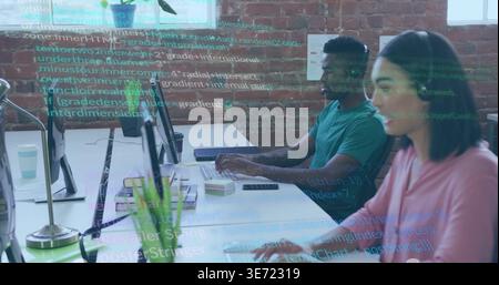 Typing coworkers in pink blouse, teal t-shirt, coding on monitors at open office with code overlay. Teamwork, programming, developers, screens, desk, Stock Photo