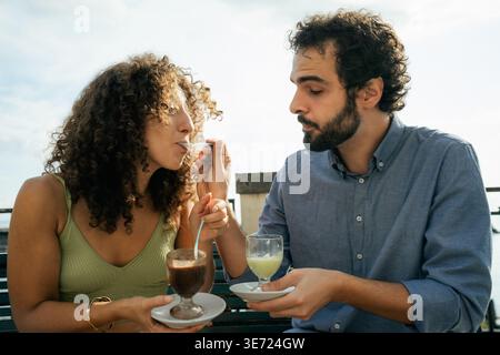 Young couple enjoying dessert together while smiling and spending relaxed time outdoors on a sunny day Stock Photo