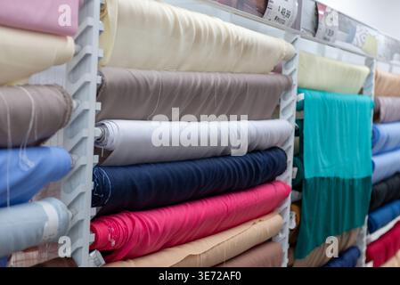 Close-up of various colorful rolls of textile fabric stacked on a shelf in a shop or store. Stock Photo
