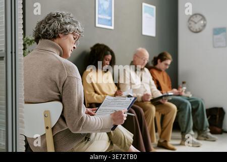 Senior Woman Completing Intake Form in Medical Waiting Room Stock Photo