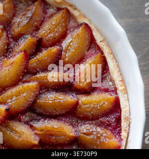 Freshly baked homemade plum tart with caramelized fruit slices in a white ceramic mold, selective focus. Delicious seasonal dessert Stock Photo