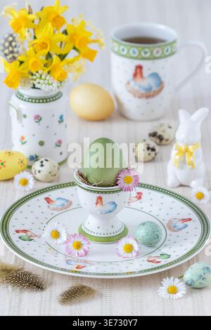 table arrangement with a naturally dyed eggs, porcelain with easter ornament and bouquet of narcissus Stock Photo