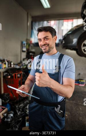 Car mechanic holding tablet and showing thumbs up in auto repair shop Stock Photo