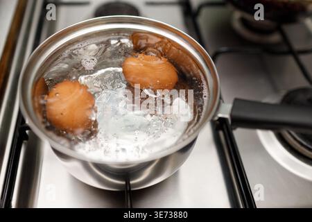 Saucepan stainless steel with boiling eggs breakfast in water on gas stove. Stock Photo