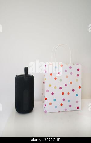 Portable speaker next to colorful gift bag on white background, modern lifestyle and gift concept. Stock Photo