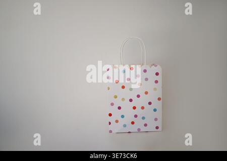 Cute polka dot gift bag on neutral background, minimal festive packaging for presents and celebrations. Stock Photo