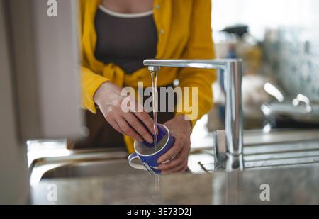 Woman washing ceramic mug in kitchen sink. Stock Photo