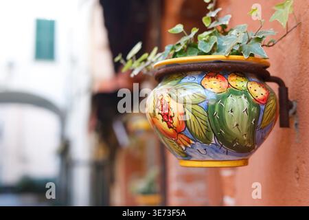 Traditional hand painted Italian ceramic flower pot with ivy on terracotta wall. Close-up shot features colorful Mediterranean pottery with Stock Photo