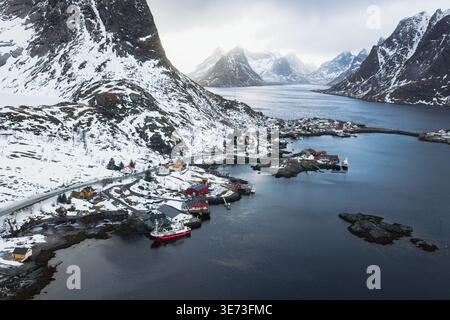 Aerial view of Reinebringen, Norway, where snow-dusted mountains meet the icy fjord, casting long shadows over the quaint village below, Reinebringen, Stock Photo