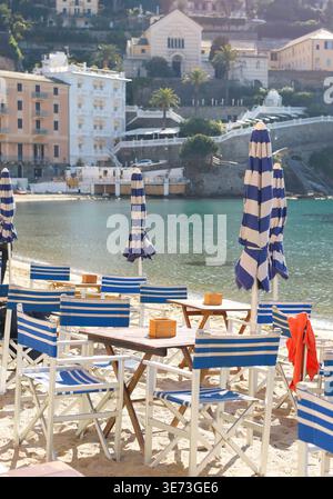 Traditional Italian beach club with blue striped chairs and umbrellas on sandy shore with copy space. Vertical shot features turquoise sea and Stock Photo