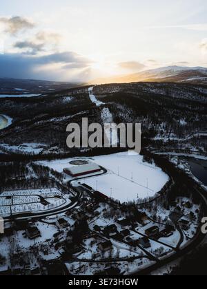 Aerial view of snow-covered fields meet dark forests under a sky streaked with golden sunset hues, casting long shadows over the landscape, Sjøvegan, Stock Photo