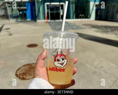 Surrey, BC - April 9, 2026: A close-up of a person holding a refreshing Jollibee pineapple quencher drink in a clear plastic cup outdoors. Stock Photo