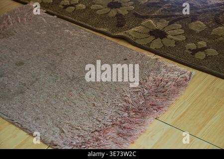 Worn pink shaggy rug and floral patterned carpet on a wooden floor. Stock Photo