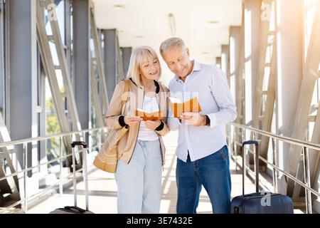 Mature couple smiling while reviewing their passports together in sunlit airport corridor Stock Photo